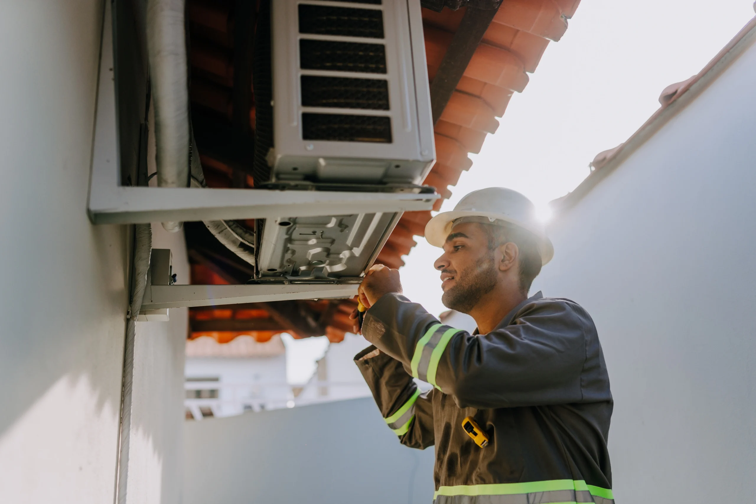 A technician in safety gear works on an outdoor air conditioning unit. 