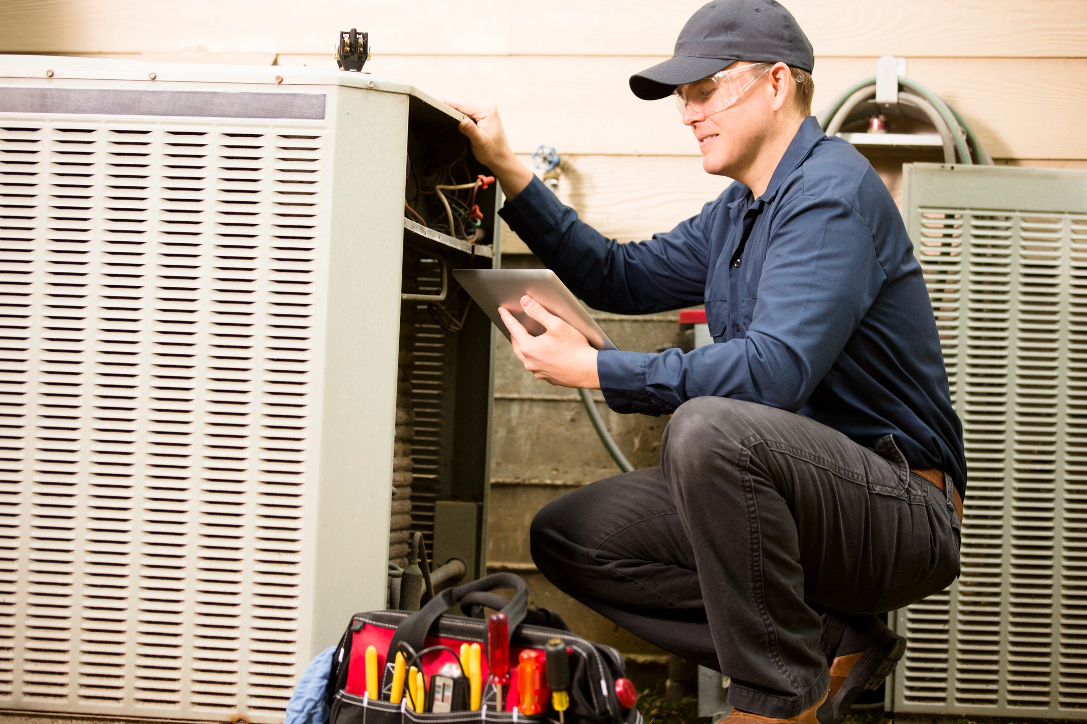 A man kneeling beside an air conditioner, inspecting or adjusting its settings.